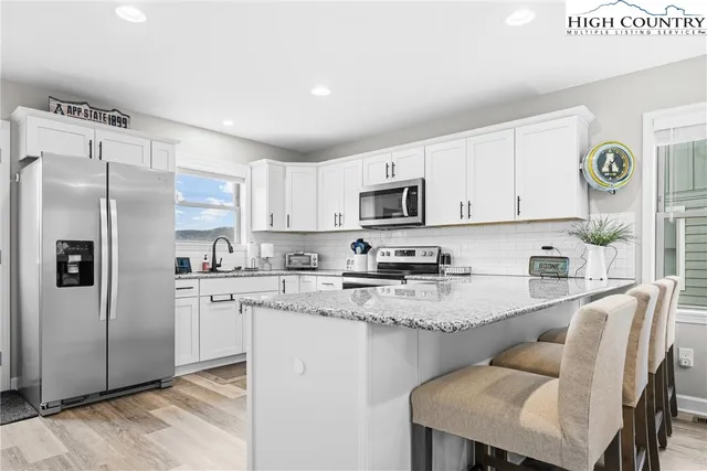 a kitchen with stainless steel appliances granite countertop a refrigerator a stove a sink dishwasher and white cabinets with wooden floor