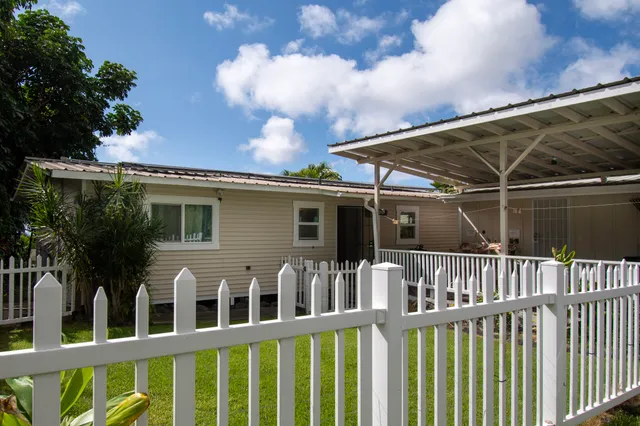 a view of a white house with a small yard and wooden fence