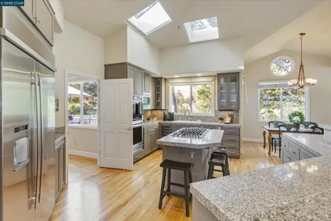 a kitchen with stainless steel appliances kitchen island granite countertop a refrigerator a stove a dining table and chairs with wooden floor