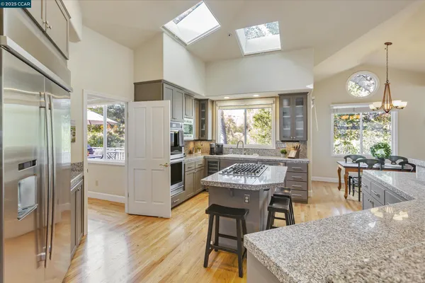 a kitchen with stainless steel appliances kitchen island granite countertop a refrigerator a stove a dining table and chairs with wooden floor