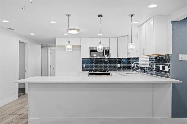 a kitchen with stainless steel appliances granite countertop a sink a stove a refrigerator a center island a stove and white cabinets with wooden floor