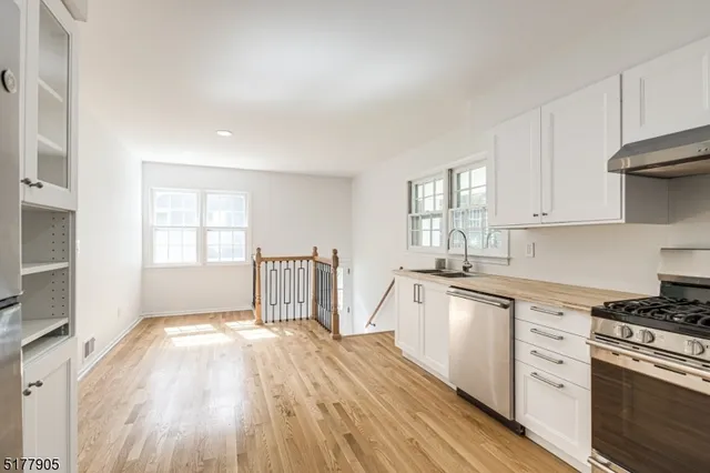a kitchen with granite countertop a stove a sink and white cabinets with wooden floor