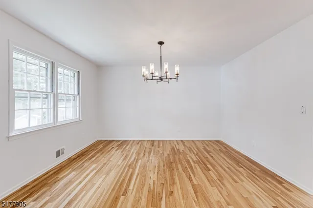 a view of empty room with wooden floor and chandelier