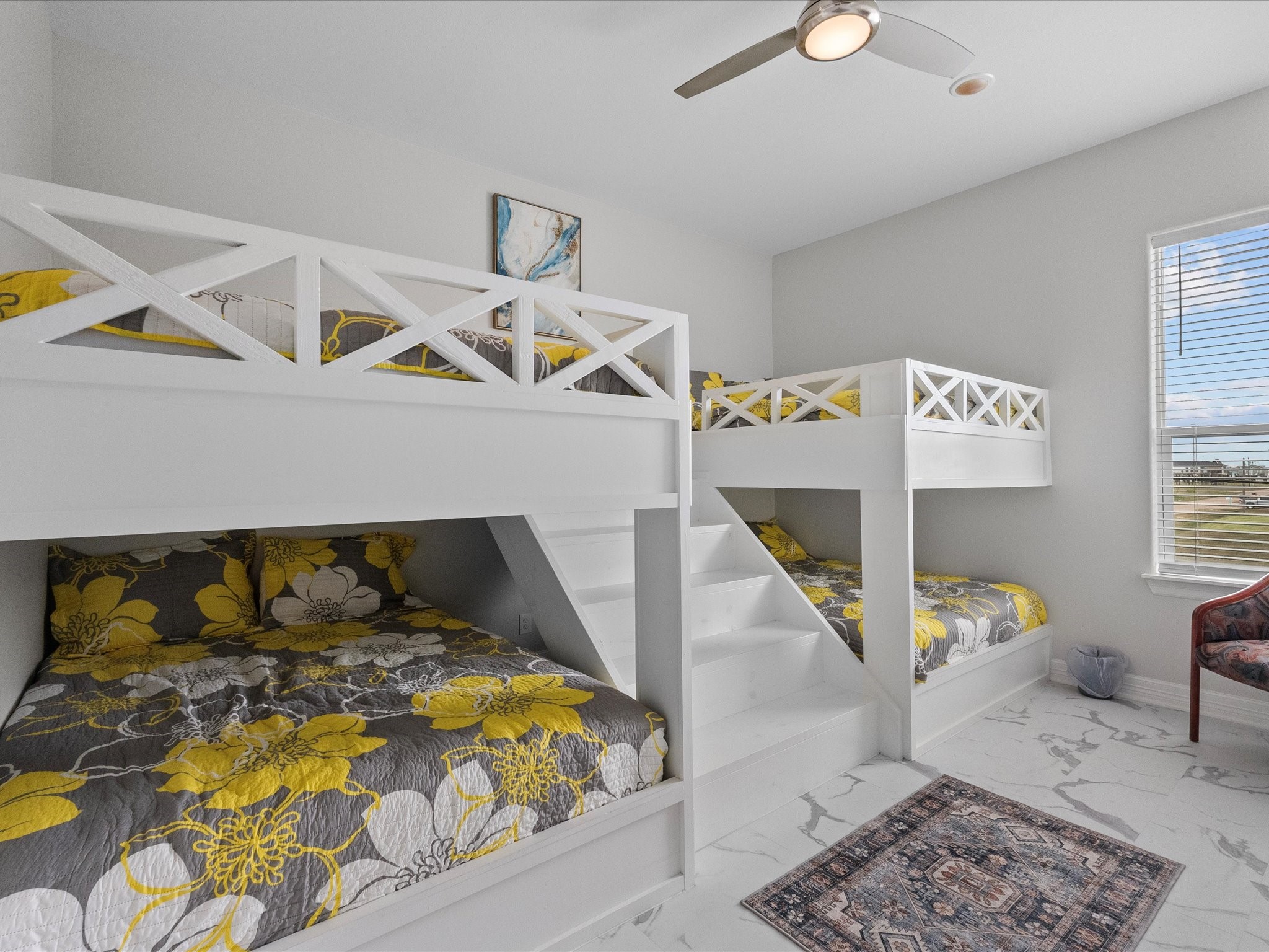 1018 Seashell Drive Surfside Beach, TX 77541 - Photo 29 of 49 This bright and airy bedroom features two sets of stylish white bunk beds with floral bedding, a ceiling fan, large window for natural light, and modern marble flooring. Perfect for accommodating multiple guests comfortably.