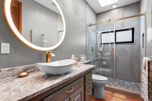 a bathroom with a granite countertop sink a toilet a mirror and shower