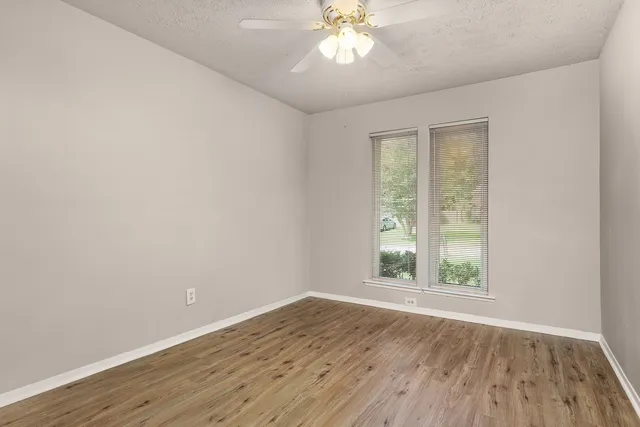 an empty room with wooden floor fan and windows