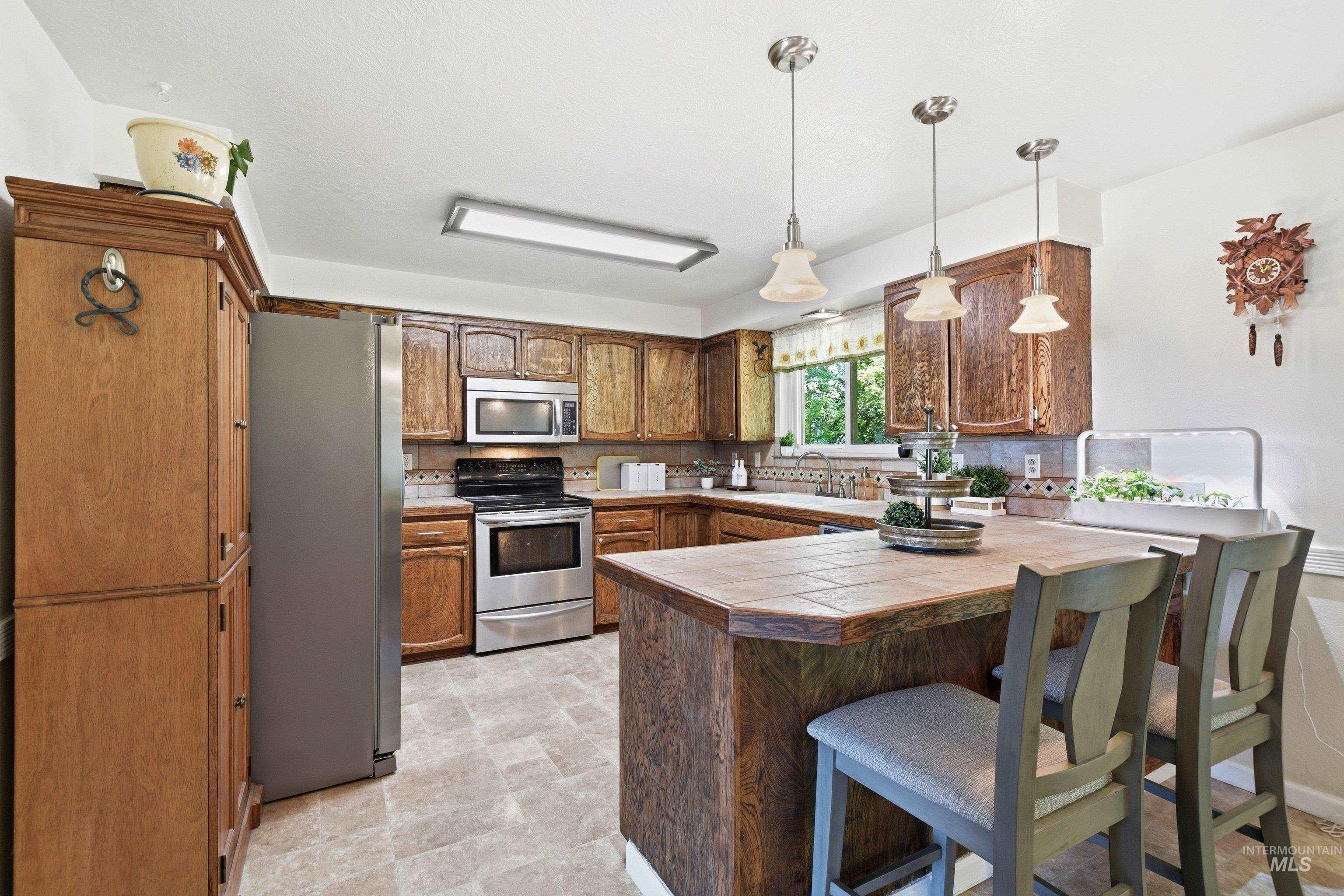15095 David Street Caldwell, ID 83607 - Photo 14 of 39 Well-appointed kitchen featuring wood cabinetry, stainless steel appliances, and a tiled countertop island with pendant lighting