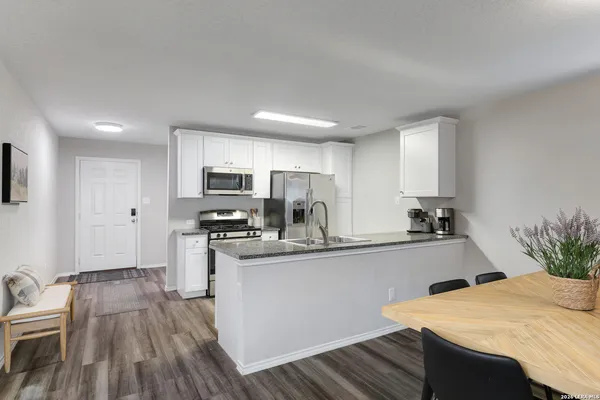 a kitchen with stainless steel appliances a sink a stove a refrigerator white cabinets and wooden floor