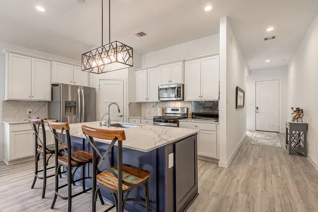 a kitchen with stainless steel appliances a dining table chairs stove refrigerator and cabinets