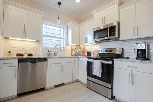 a kitchen with stainless steel appliances granite countertop white cabinets a sink a stove a microwave and wooden floors