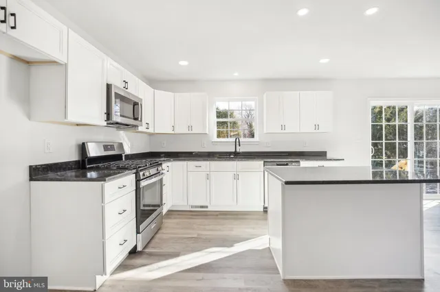 a kitchen with stainless steel appliances granite countertop a stove a sink and white cabinets