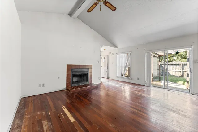 an empty room with wooden floor fireplace and windows