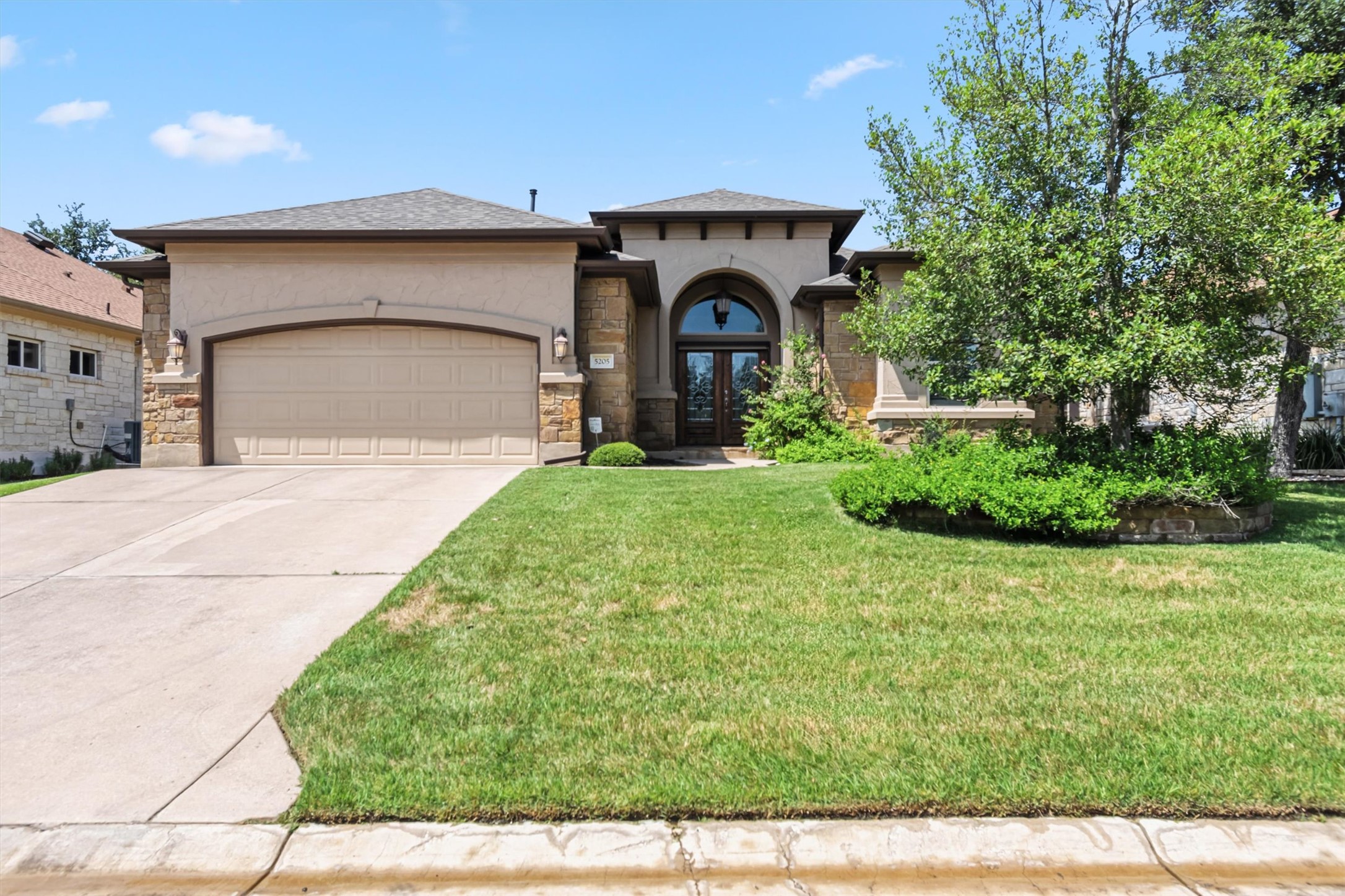 View of front of home with french doors, an attached garage, a front yard, driveway, and stone siding