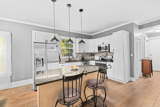 a kitchen with kitchen island granite countertop a refrigerator a stove a dining table and chairs with wooden floor