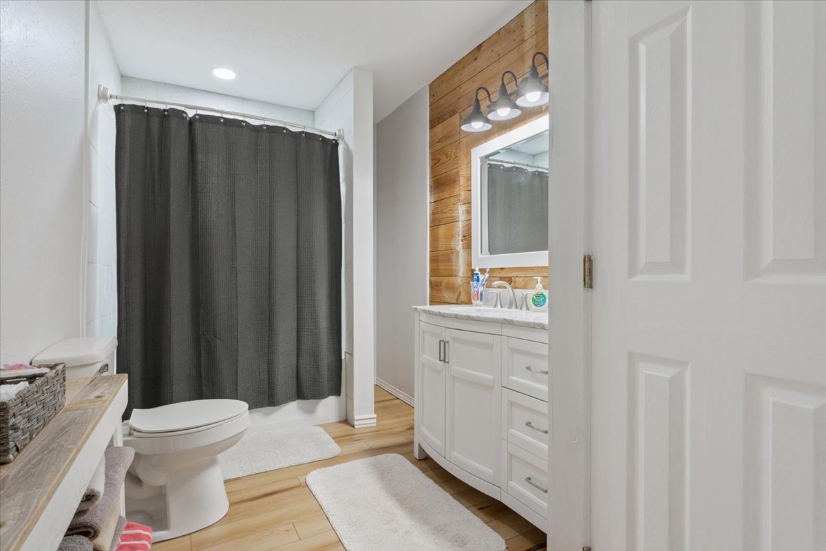 1607 North Harding Avenue Cameron, TX 76520 - Photo 28 of 37 A well-lit bathroom features light wood flooring and a modern vanity against a rustic wood-paneled accent wall.