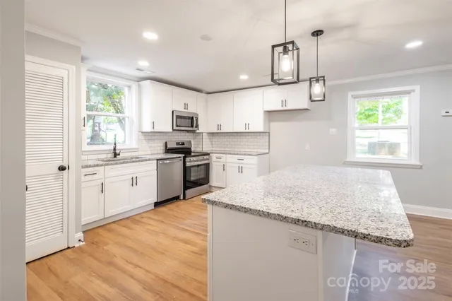 a kitchen with stainless steel appliances granite countertop a sink dishwasher a refrigerator and white cabinets with wooden floor
