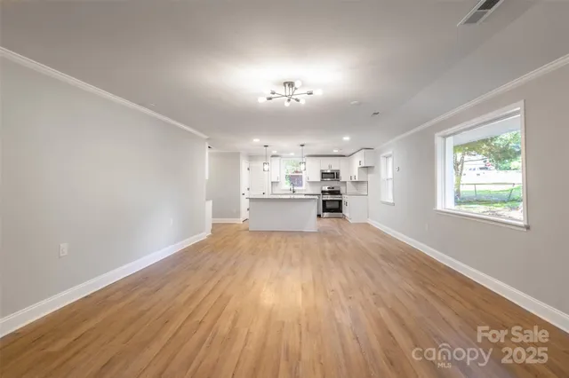 an empty room with wooden floor kitchen view and windows