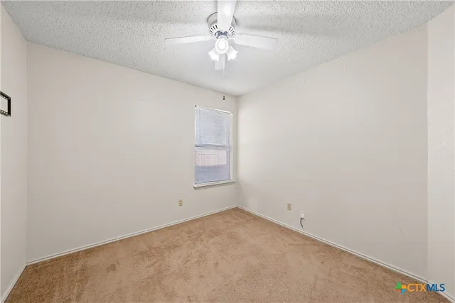 an empty room with a chandelier fan and windows