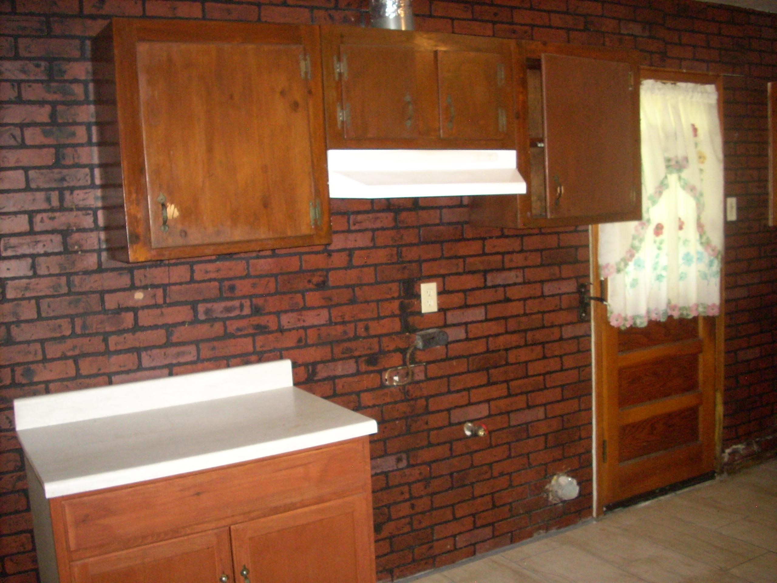 4282 Westmont Road Memphis, TN 38109 - Photo 15 of 15 Brick-patterned wall texture featuring wood-finish cabinetry, a white countertop, and a wood-panel door