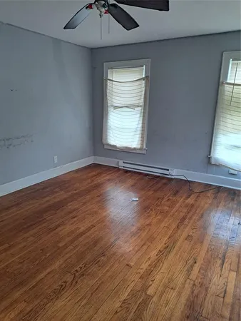 an empty room with wooden floor chandelier fan and windows