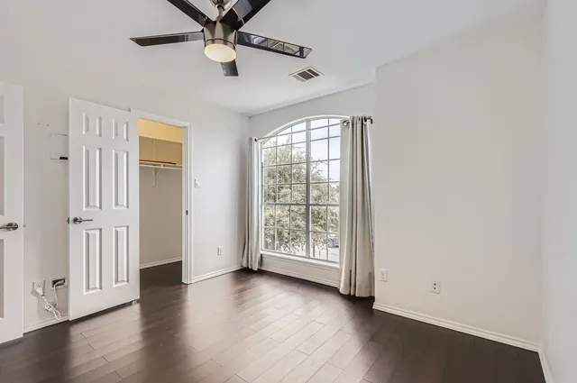 an empty room with wooden floor fan and windows