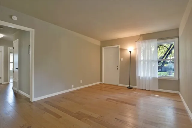 a view of an empty room with window and wooden floor