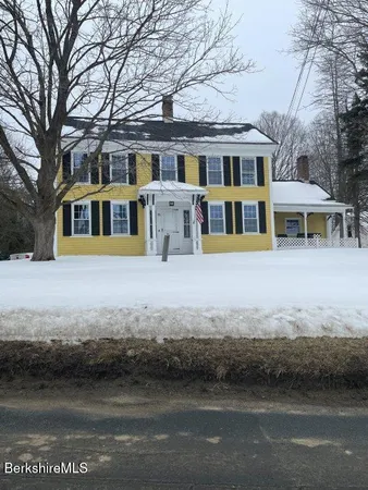 a front view of a building with a yard and large trees