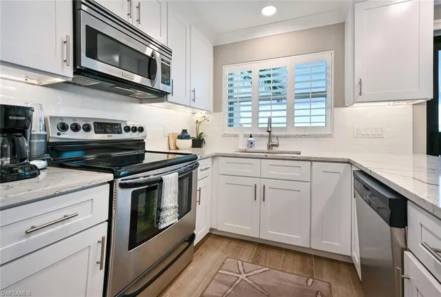 a kitchen with stainless steel appliances granite countertop white cabinets a sink a stove a microwave and wooden floors