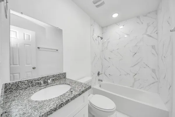 a bathroom with a granite countertop sink a toilet a mirror a bathtub and shower