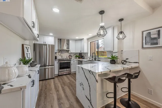 a kitchen with stainless steel appliances granite countertop a sink a stove a refrigerator cabinets and chairs