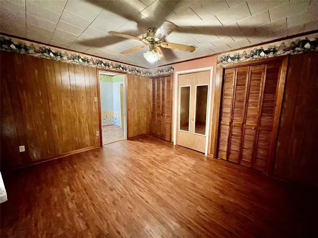 a view of an empty room with wooden floor and a ceiling fan