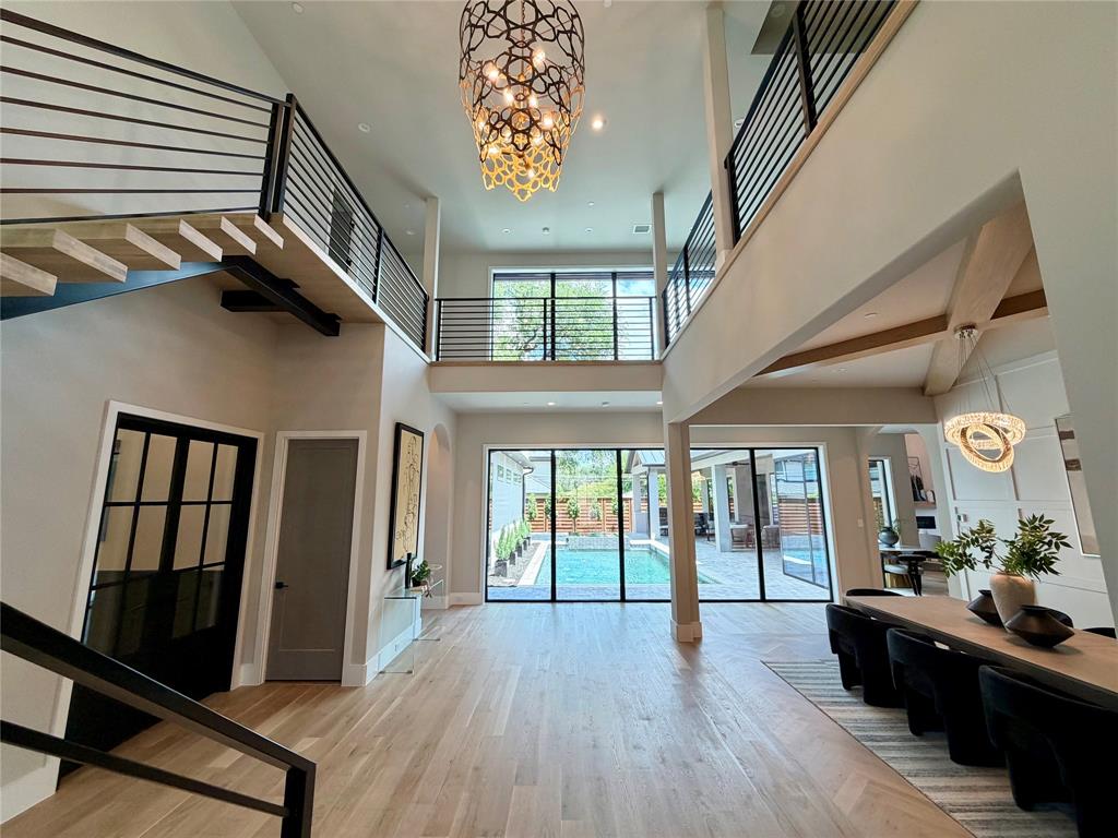 11028 Edgemere Road Dallas, TX 75230 - Photo 8 of 40 Two-story foyer featuring light wood-finish flooring, a contemporary chandelier, open-tread staircase with metal railing, and floor-to-ceiling glass doors opening to a backyard pool