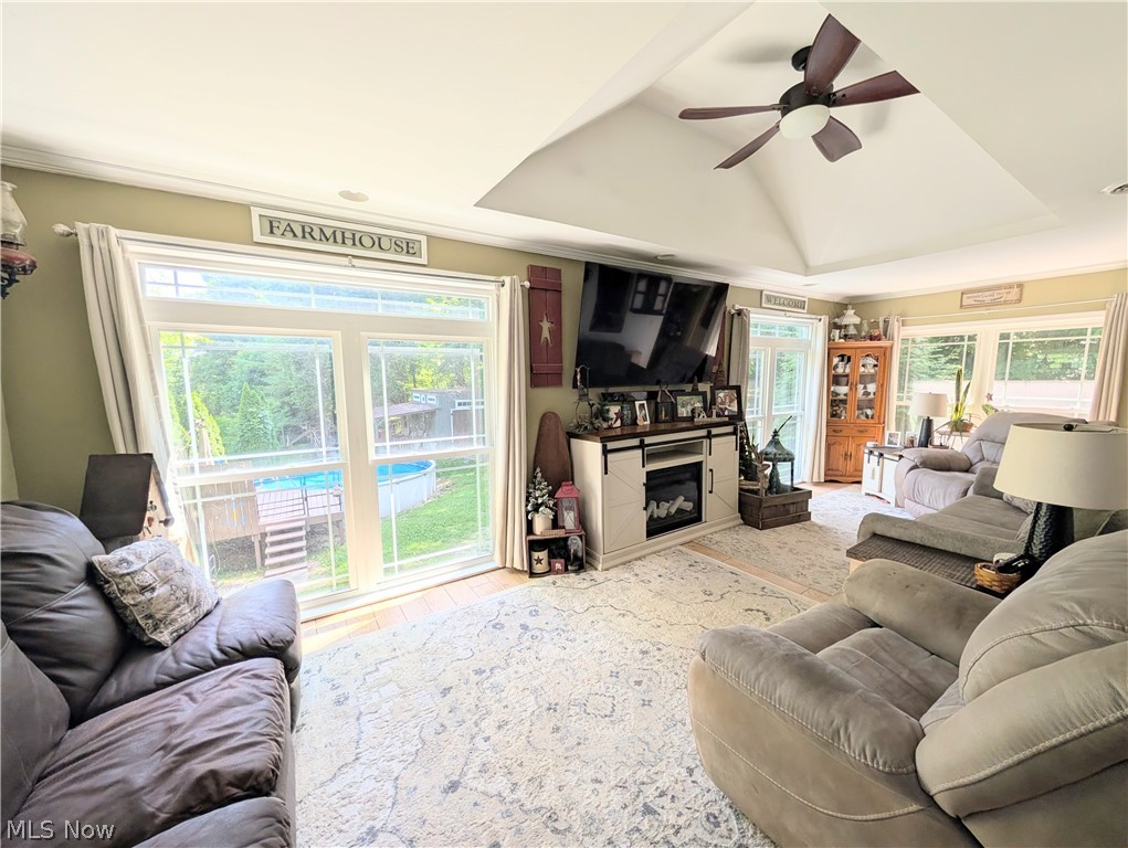 6700 McCaslin Road Nashport, OH 43830 - Photo 15 of 30 Living space featuring a tray ceiling with a ceiling fan, a built-in electric fireplace media console, hardwood-finish flooring, and multiple windows providing natural light and exterior views