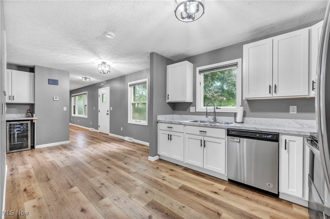 5306 Lockwood Road Madison, OH 44057 - Photo 11 of 28 Kitchen featuring white cabinetry, wine cooler, sink, stainless steel dishwasher, and light hardwood / wood-style floors