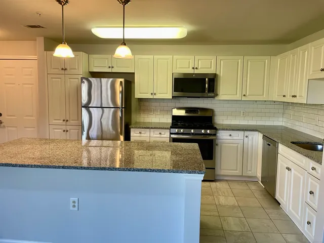 a kitchen with kitchen island granite countertop a sink a counter top space appliances and cabinets