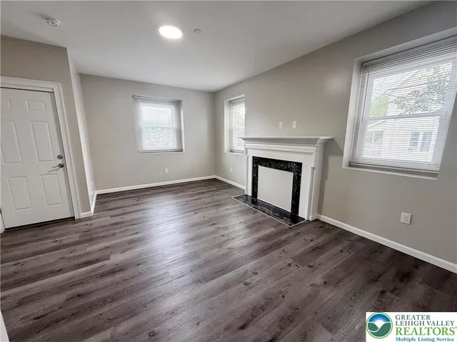 an empty room with wooden floor fireplace and windows