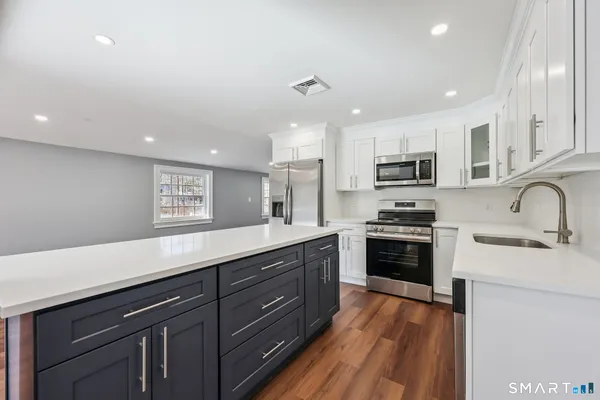 a kitchen with stainless steel appliances granite countertop a sink a stove top oven a refrigerator with wooden floors and cabinets