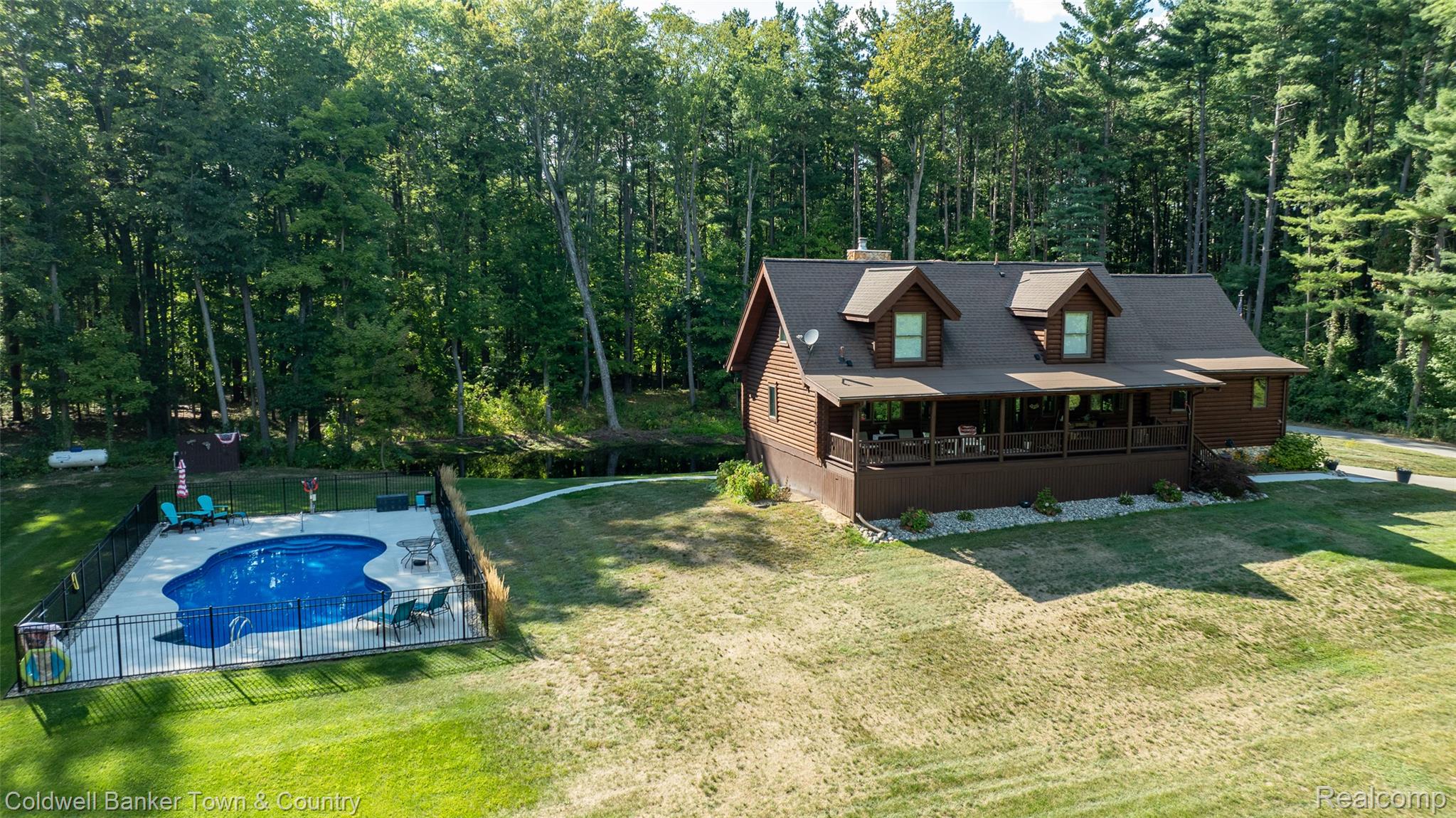 7023 Munsell Road Howell, MI 48843 - Photo 7 of 55 Wood-sided home with dormer windows, a covered front porch, and a fenced swimming pool