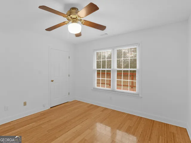 a view of an empty room with wooden floor and a ceiling fan