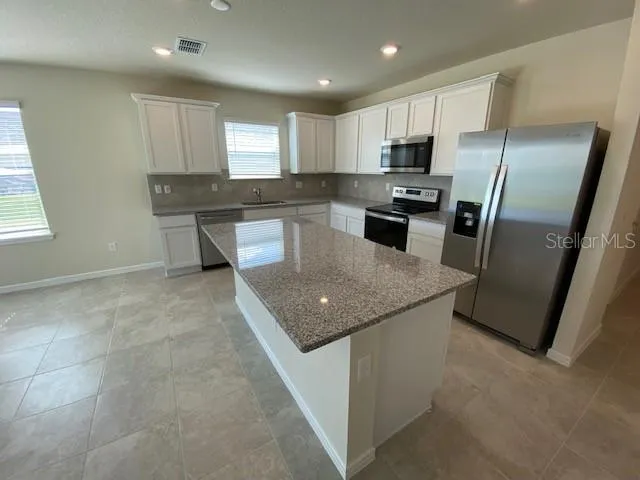 a kitchen with granite countertop a refrigerator a sink a stove a microwave a counter top and cabinets