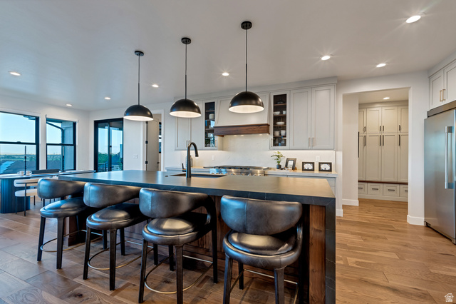 2145 North Main Street Centerville, UT 84014 - Photo 14 of 53 Kitchen featuring glass insert cabinets, high quality fridge, pendant lighting, light wood-style floors, and a breakfast bar