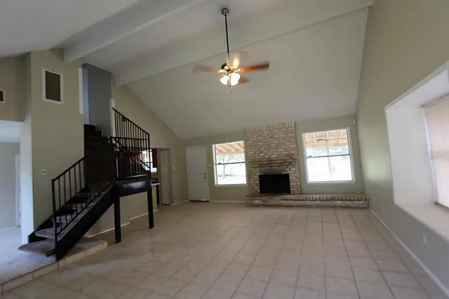 a view of a livingroom with a fireplace a ceiling fan and windows