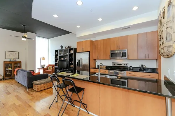 a kitchen with stainless steel appliances kitchen island granite countertop a stove top oven a sink a dining table and chairs with wooden floor