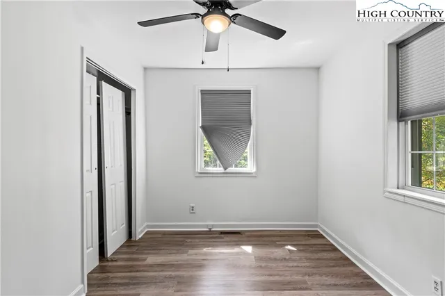 an empty room with wooden floor fan and windows