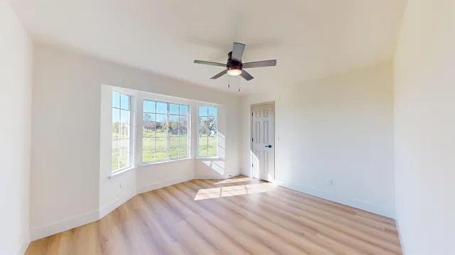 a view of empty room with wooden floor and fan