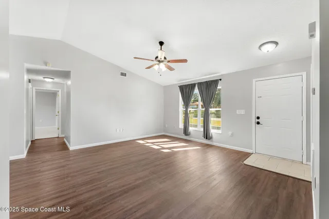 an empty room with wooden floor ceiling fan and window
