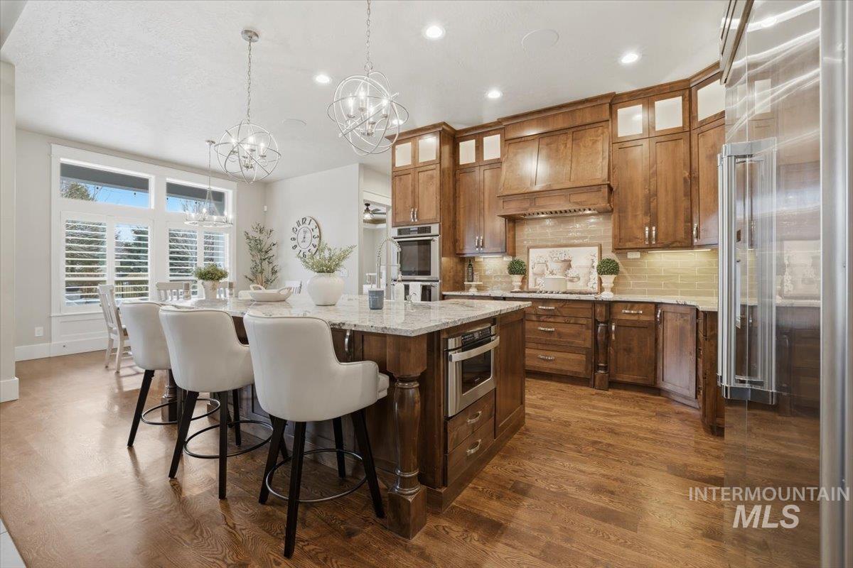 6590 North Fairborn Avenue Meridian, ID 83646 - Photo 20 of 49 Kitchen featuring stainless steel appliances, light stone countertops, hanging light fixtures, decorative backsplash, and a breakfast bar