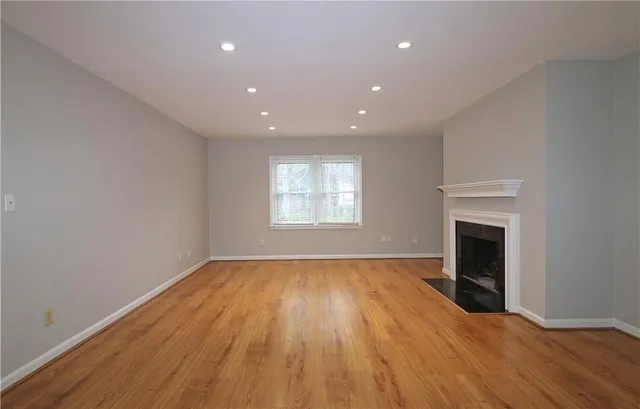 a view of an empty room with wooden floor fireplace and a window