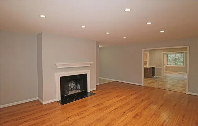 a view of an empty room with wooden floor fireplace and a window