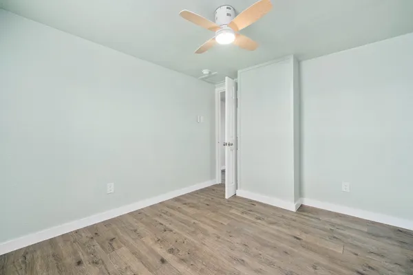 a view of an empty room with wooden floor and a ceiling fan